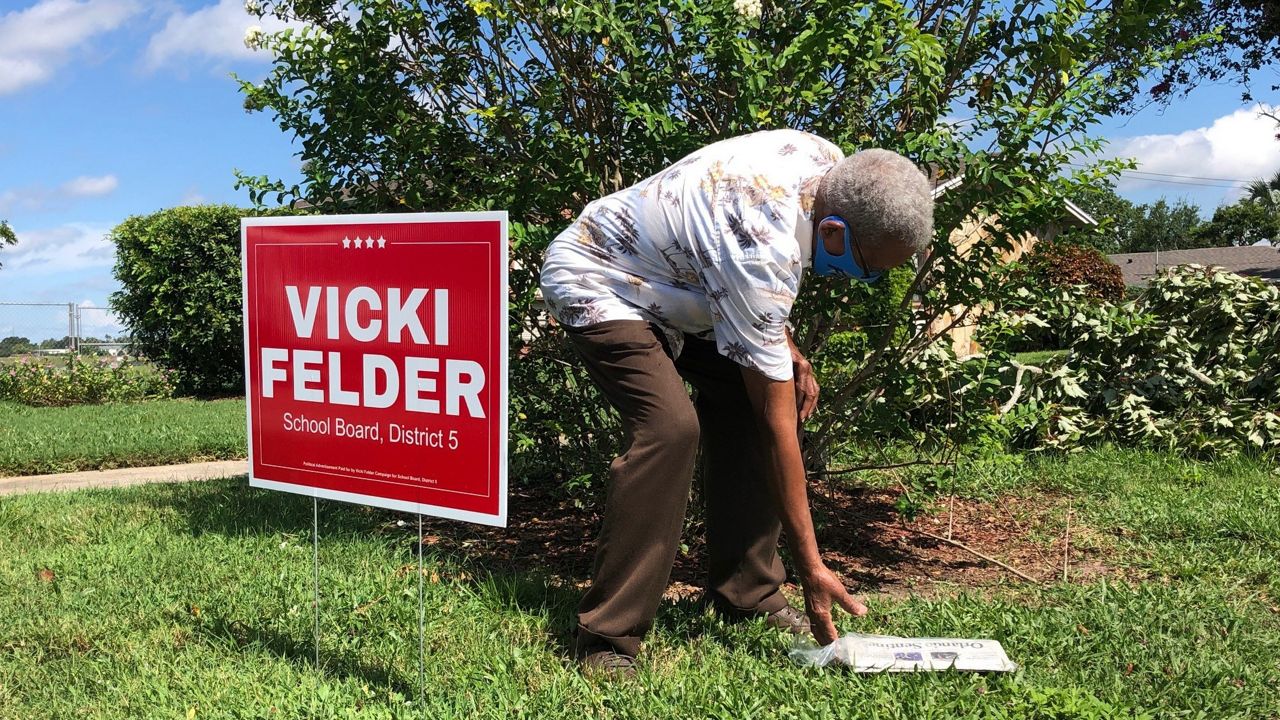 Ulysses Floyd picks up his newspaper at his Orlando home, where the lawn is dotted with campaign signs. (Julie Gargotta, Spectrum News)