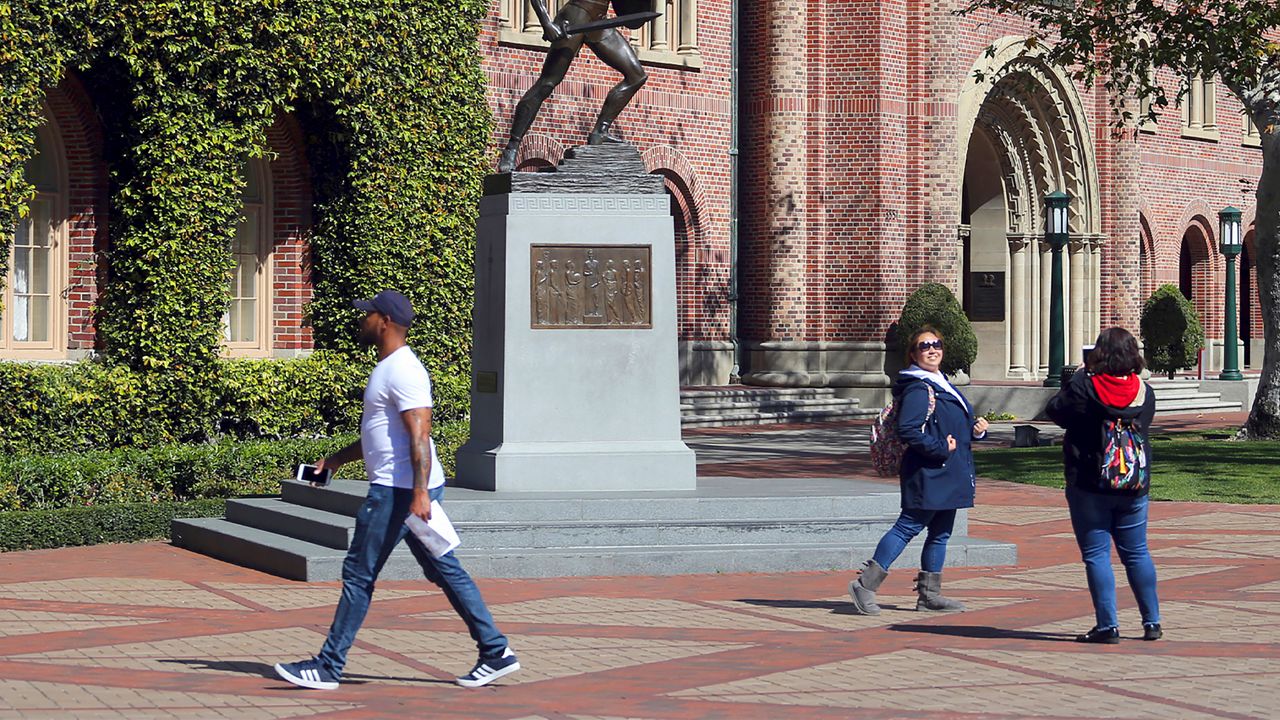 In this March 12, 2019 file photo, people pose for photos in front of the iconic Tommy Trojan statue on the campus of the University of Southern California in Los Angeles. USC will phase in free tuition for students from families with an annual income of $80,000 or less, USC President Carol L. Folt announced Thursday, Feb. 20, 2020. As part of the initiative, ownership of a home will not be counted in determining a student's financial need. (AP Photo/Reed Saxon, File)