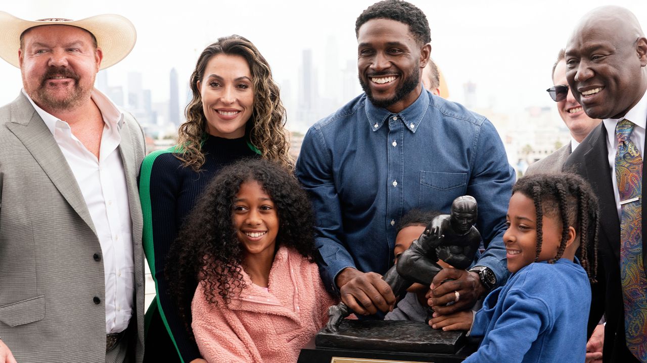 Former USC football player Reggie Bush poses with his attorneys, left, Levi McCathern and Ben Crump, right, along with his family and Heisman trophy during a news conference at the Los Angeles Memorial Coliseum on Thursday. (AP Photo/Richard Vogel)