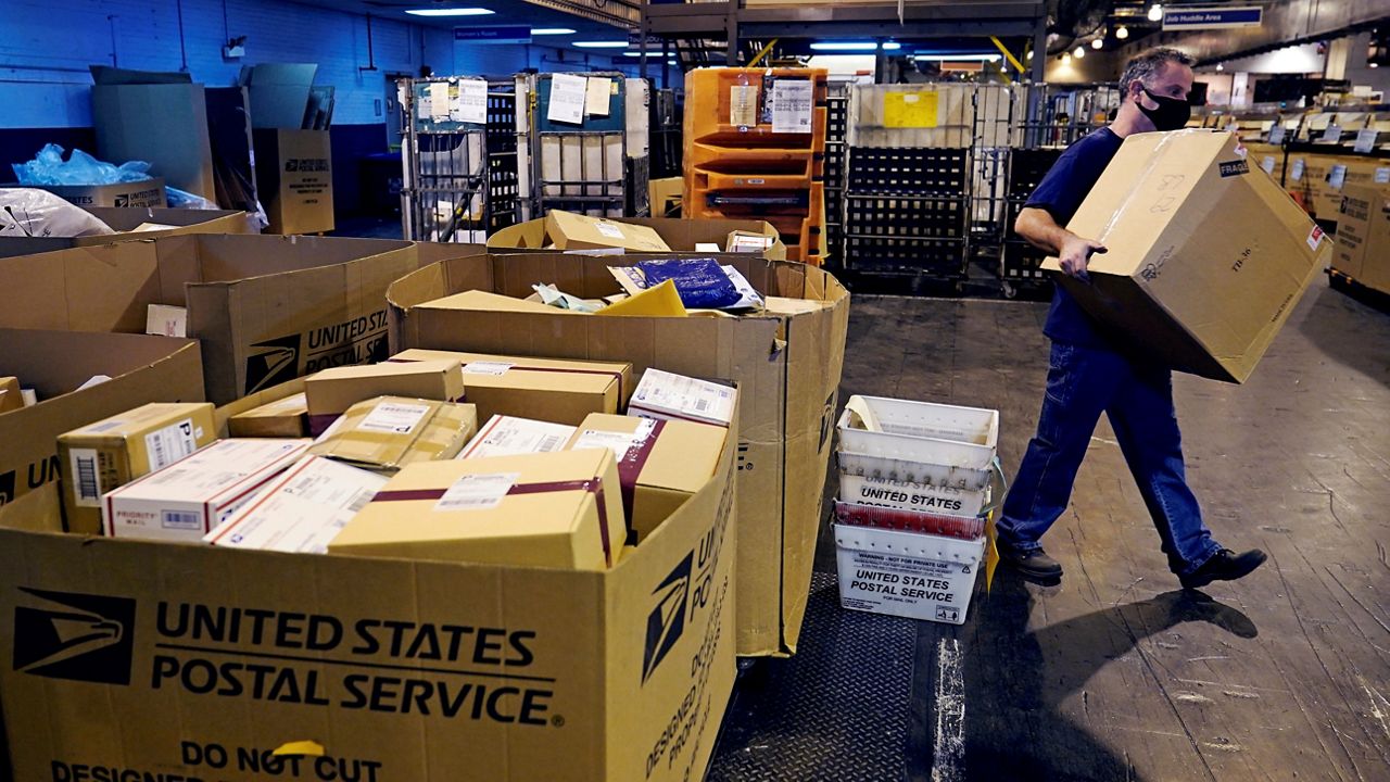 A worker carries a large parcel at the United States Postal Service sorting and processing facility, Thursday, Nov. 18, 2021, in Boston.