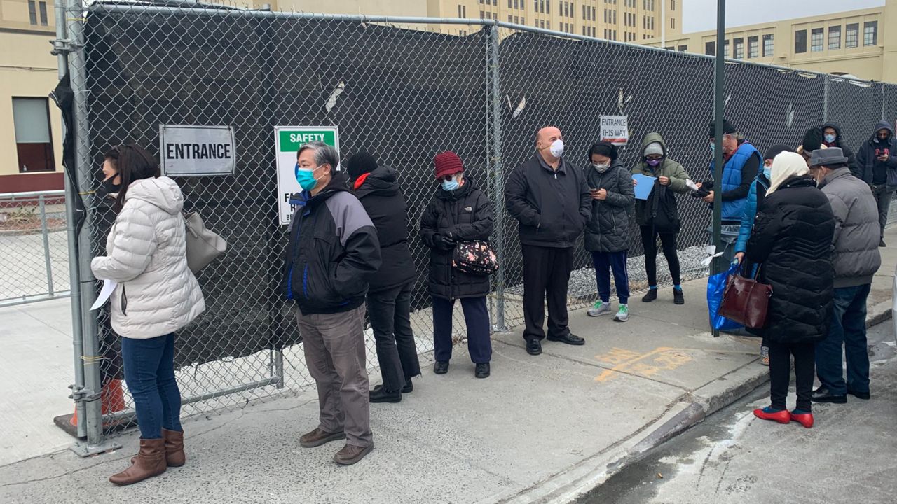 Several people stand in line outside the Brooklyn Army Terminal.