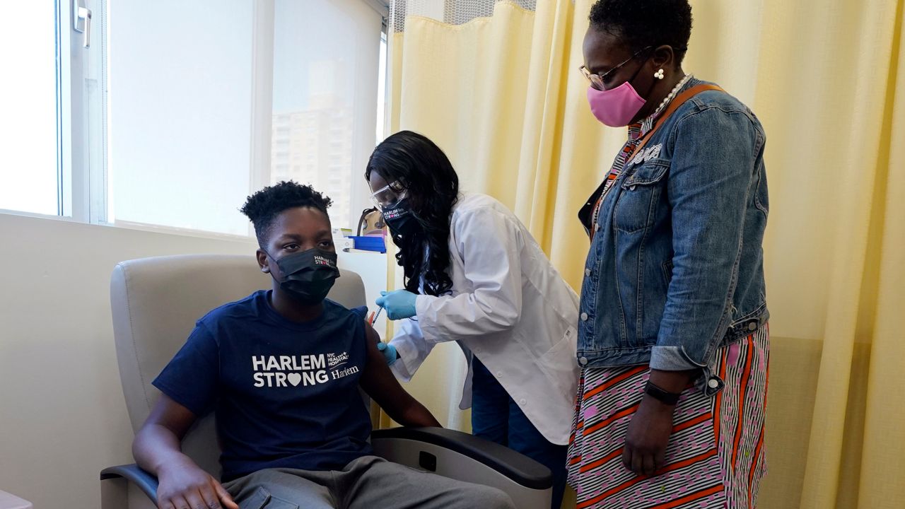 Julian Boyce, 14, receives a vaccine dose at a city clinic in Harlem as his mother looks on, May 13, 2021. (AP Photo/Richard Drew)