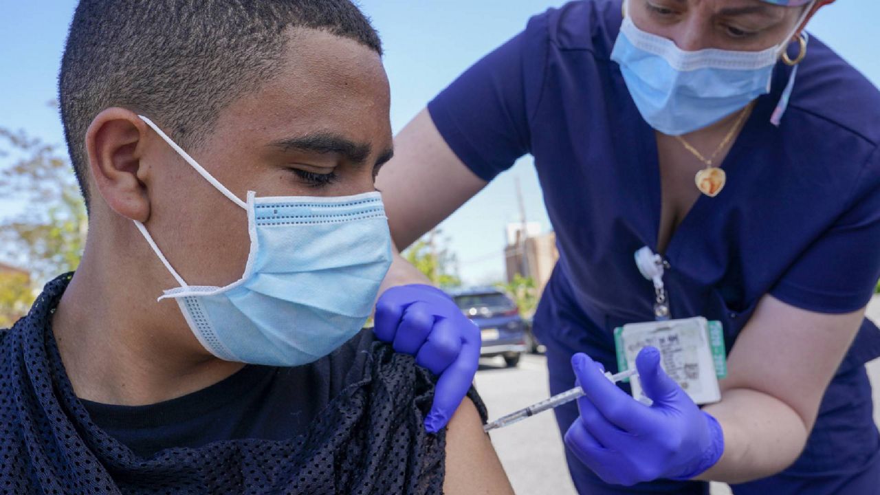 Justin Bishop, 13, watches as Registered Nurse Jennifer Reyes inoculates him with the first dose of the Pfizer COVID-19 vaccine at the Mount Sinai South Nassau Vaxmobile parked at the De La Salle School, Friday, May 14, 2021, in Freeport, N.Y. (AP Photo/Mary Altaffer)