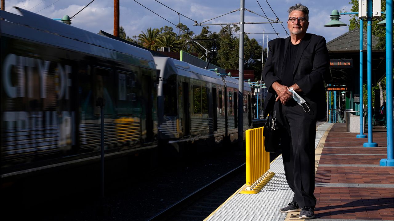 In this April 27, 2021, photo Brad Hudson poses as a Los Angeles Metro train goes by in South Pasadena, Calif. As President Joe Biden urges more federal spending for public transportation, transit agencies decimated by COVID-19 are struggling with a new uncertainty: how to win passengers back. (AP Photo/Mark J. Terrill)