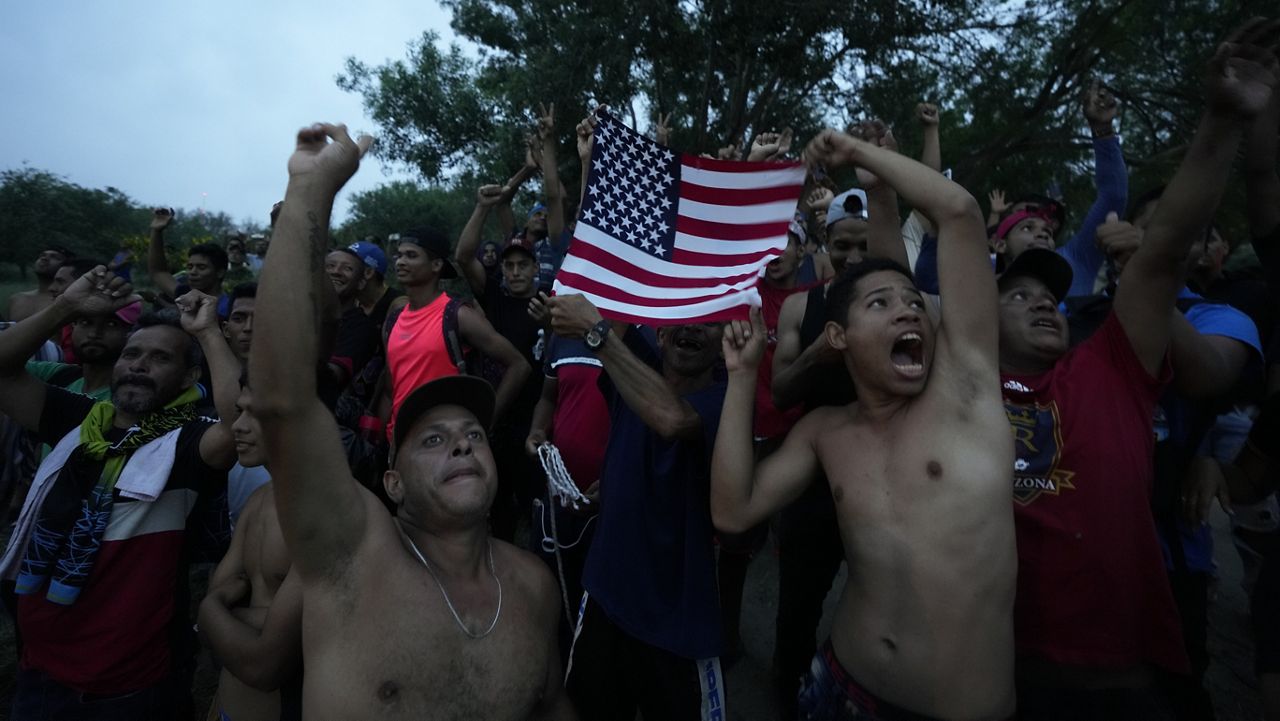 Venezuelan migrants wave a U.S. flag at a television helicopter that flew over the Rio Grande, in Matamoros, Mexico, Friday, May 12, 2023, a day after pandemic-related asylum restrictions called Title 42 were lifted. (AP Photo/Fernando Llano)