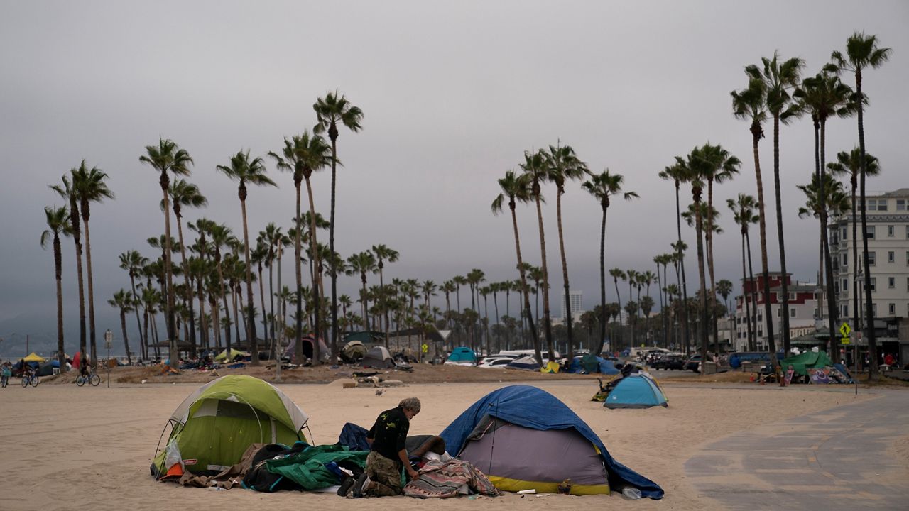 A homeless man goes through his belongings outside his tent pitched on the beach on June 29, 2021, in the Venice neighborhood of Los Angeles. (AP Photo/Jae C. Hong)