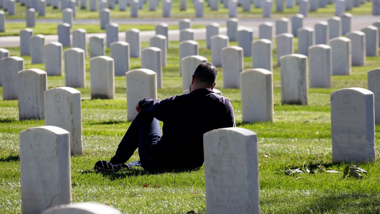 Brian Tubbs sits next to the grave of his grandfather, William Maxe, a World War II Navy veteran, during Veterans Day observances at the Los Angeles National Cemetery Wednesday, Nov. 11, 2015. (AP Photo/Nick Ut)