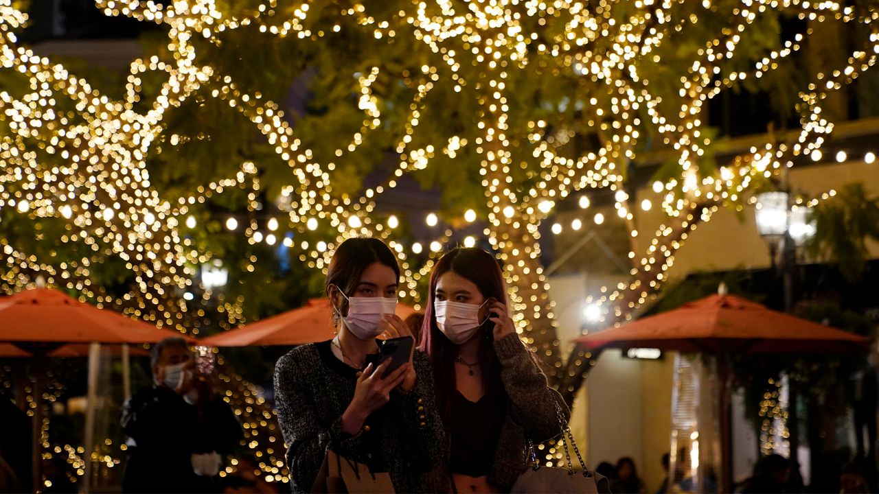 Visitors wear face masks under a tree decorated for the Christmas season amid the COVID-19 pandemic at a shopping district Wednesday, Dec. 22, 2021, in Los Angeles. (AP Photo/Marcio Jose Sanchez)