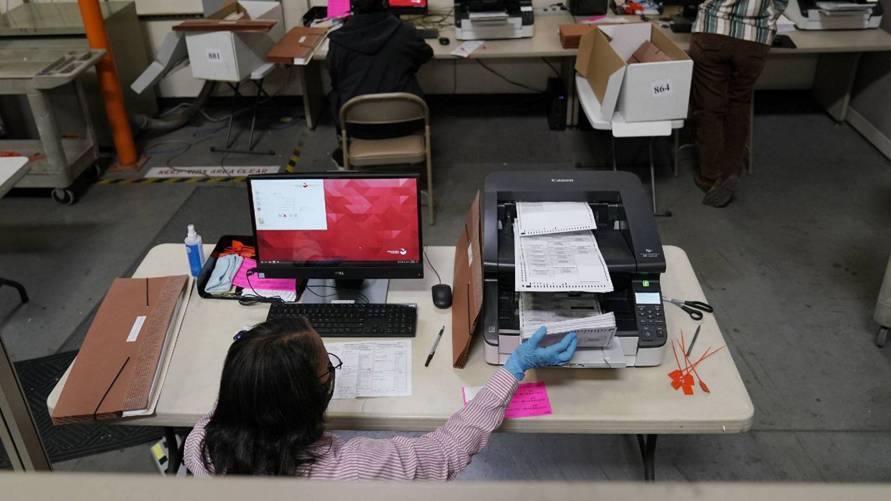 FILE - In this file photo, a county worker loads mail-in ballots into a scanner at the Clark County Election Department in Las Vegas. (AP Photo/John Locher, File)