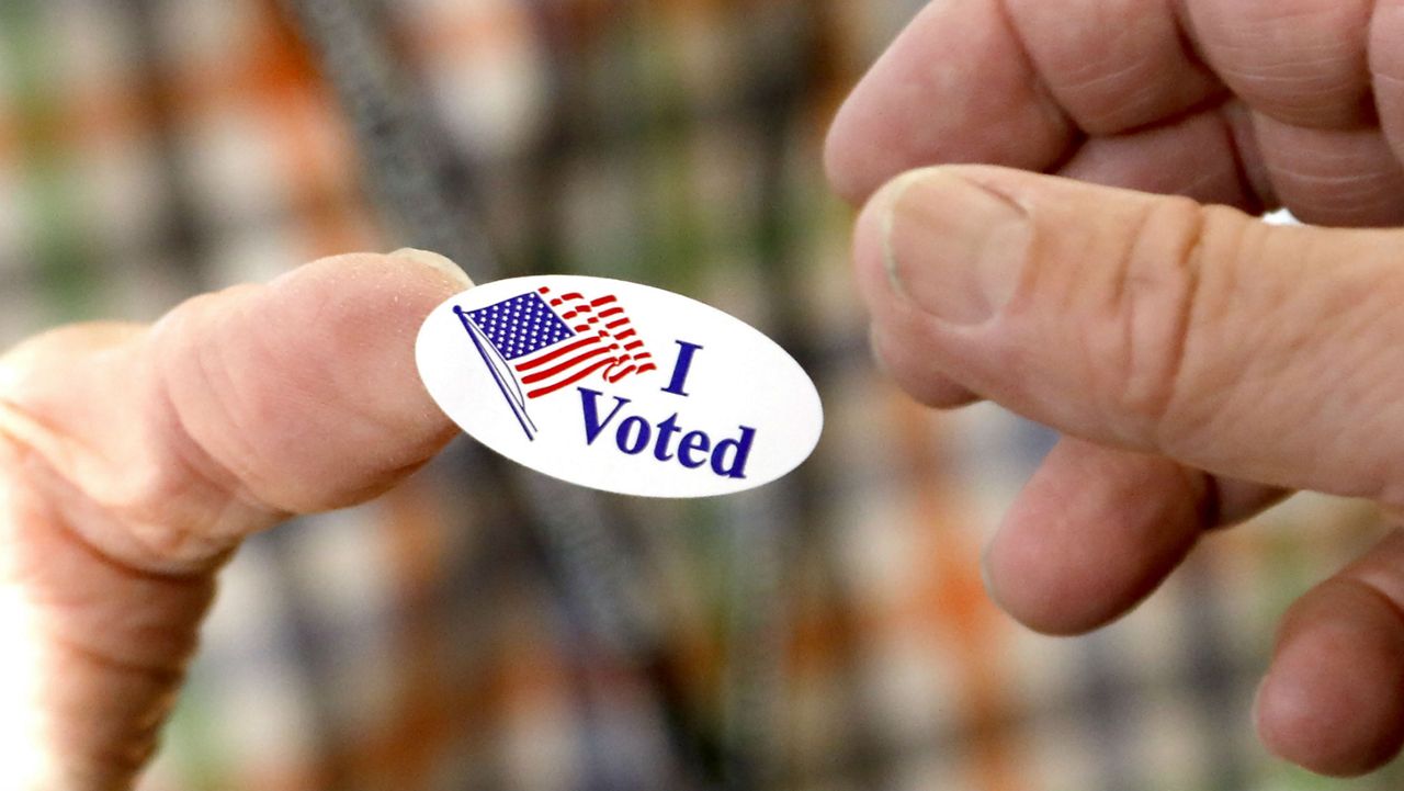 Poll worker offers a voter an "I Voted" sticker after he casts his ballot Tuesday, Nov. 5, 2019. (AP Photo/Rogelio V. Solis)