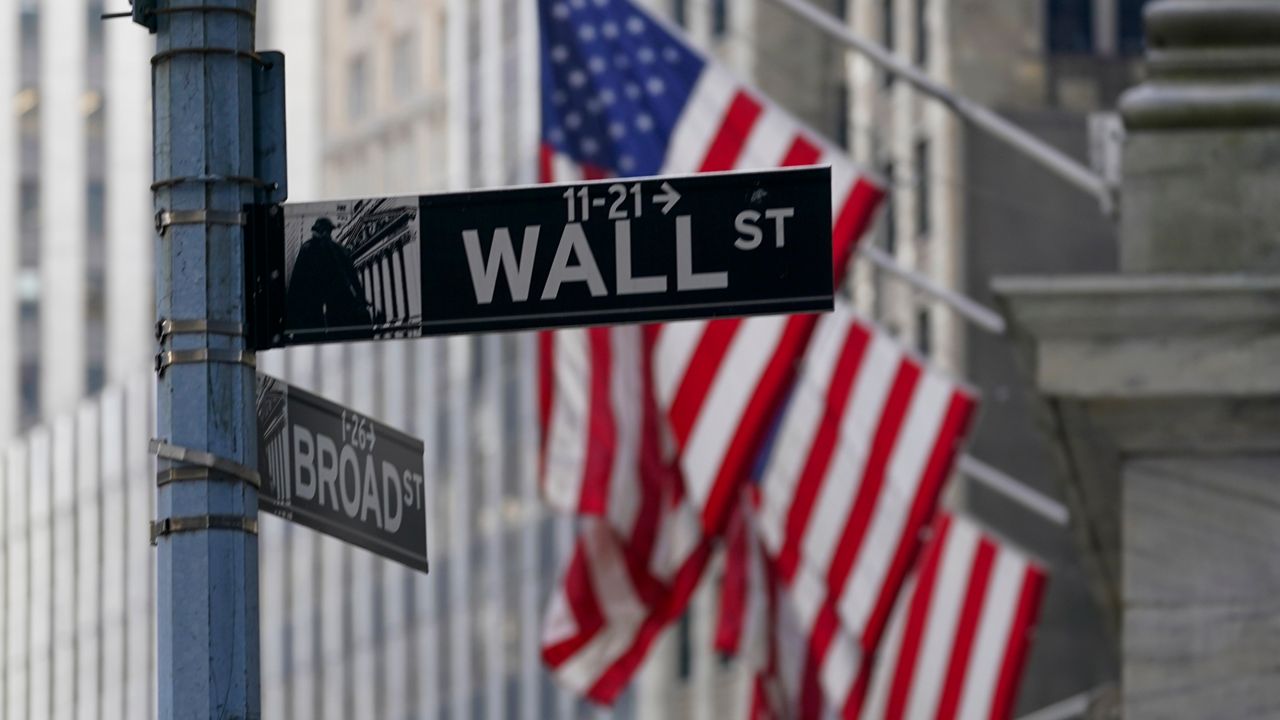 The Wall St. street sign is framed by the American flags flying outside the New York Stock exchange, Friday, Jan. 14, 2022, in the Financial District. Stocks are opening with solid gains on Wall Street Wednesday, Jan. 26, led by technology stocks after Microsoft reported standout results for its latest quarter. (AP Photo/Mary Altaffer)