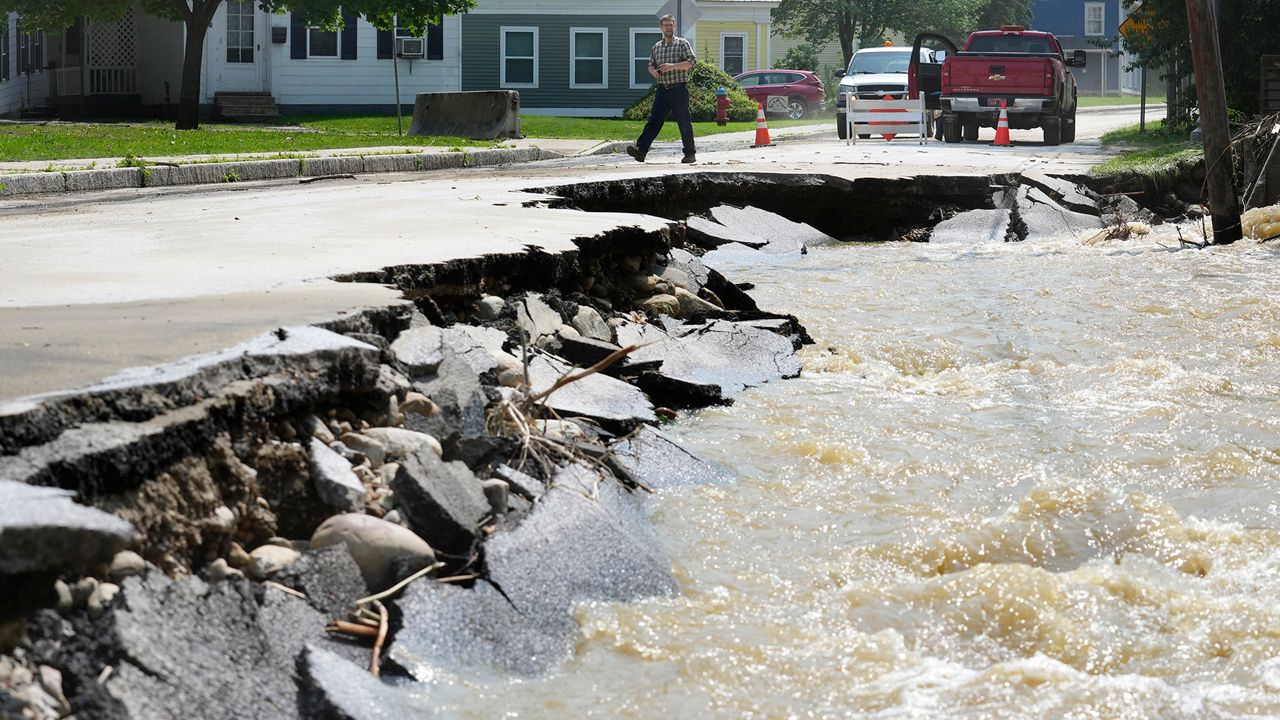 A passerby walks near a street damaged by flood waters, July 11, 2023, in Ludlow, Vt. Across the U.S., municipal water systems and sewage treatment plants are at increasing risk of damage from floods and sea-level rise brought on in part or even wholly by climate change. The storm that walloped Ludlow especially hard, damaging the picturesque ski town’s system for cleaning up sewage before it’s discharged into the Williams River. (AP Photo/Steven Senne)