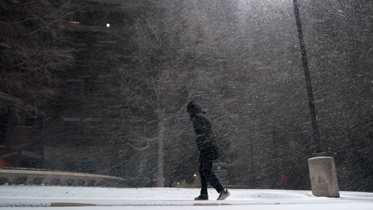 FILE - In this Feb. 14, 2021, file photo, woman walks through falling snow in San Antonio. As temperatures plunged and snow and ice whipped the state, much of Texas' power grid collapsed, followed by its water systems. Tens of millions huddled in frigid homes that slowly grew colder or fled for safety. (AP Photo/Eric Gay, File)