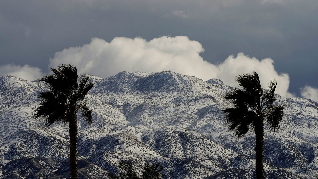 Two palms trees are backdropped by snow-covered mountains in Hesperia, Calif., Wednesday, March 1, 2023. (AP Photo/Jae C. Hong)