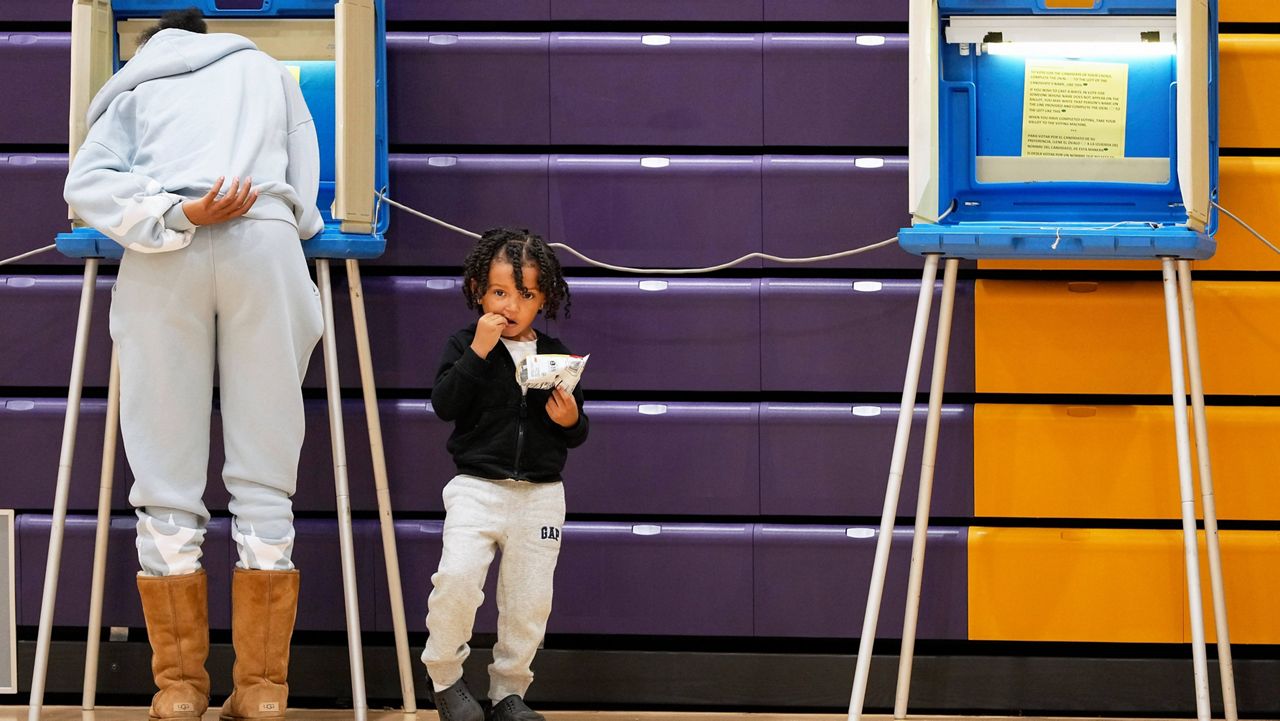 A child waits as a woman votes, Tuesday, Nov. 5, 2024, in Milwaukee, Wis. (AP Photo/Morry Gash)