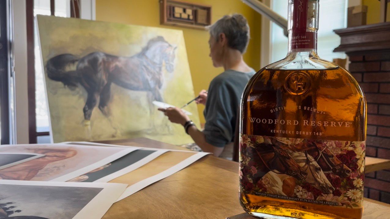 Jaime Corum paints as the bourbon bottle featuring her artwork sits on a table nearby (Spectrum News 1/Brennon Gurley