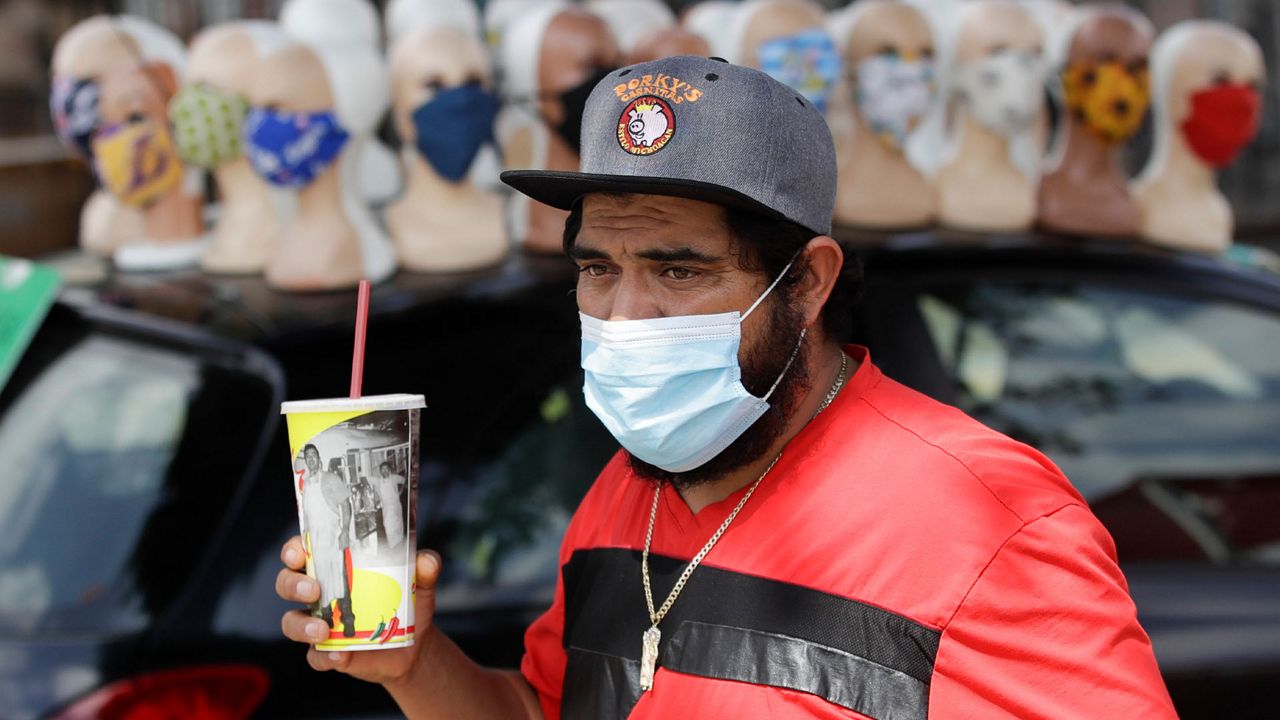 A man walks past a row of face masks for sale amid the coronavirus pandemic Monday, June 29, 2020, in Los Angeles. (AP Photo/Marcio Jose Sanchez, File)