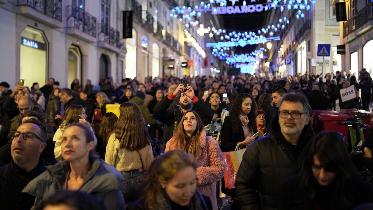 People look up at Christmas lights as crowds stroll around downtown Lisbon's Chiado neighborhood, Saturday evening, Dec. 23, 2023. (AP Photo/Armando Franca)