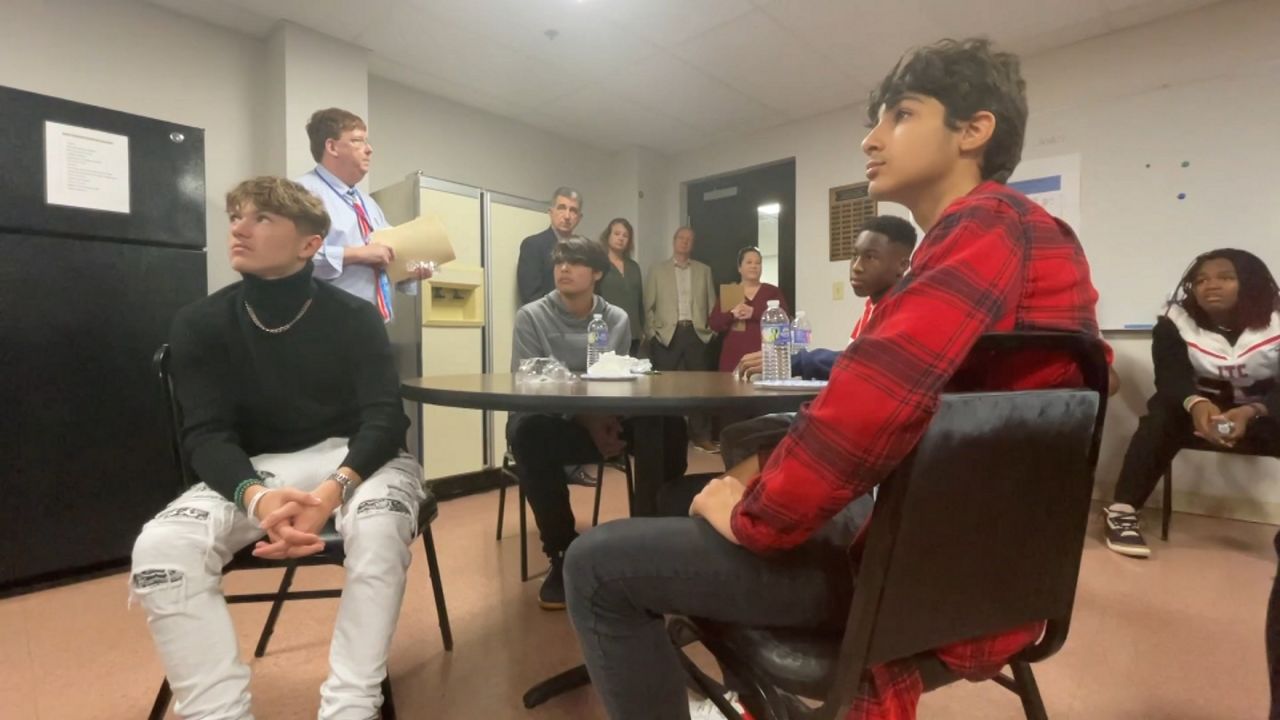 high school students sit in a break room at a school, listening to someone speak