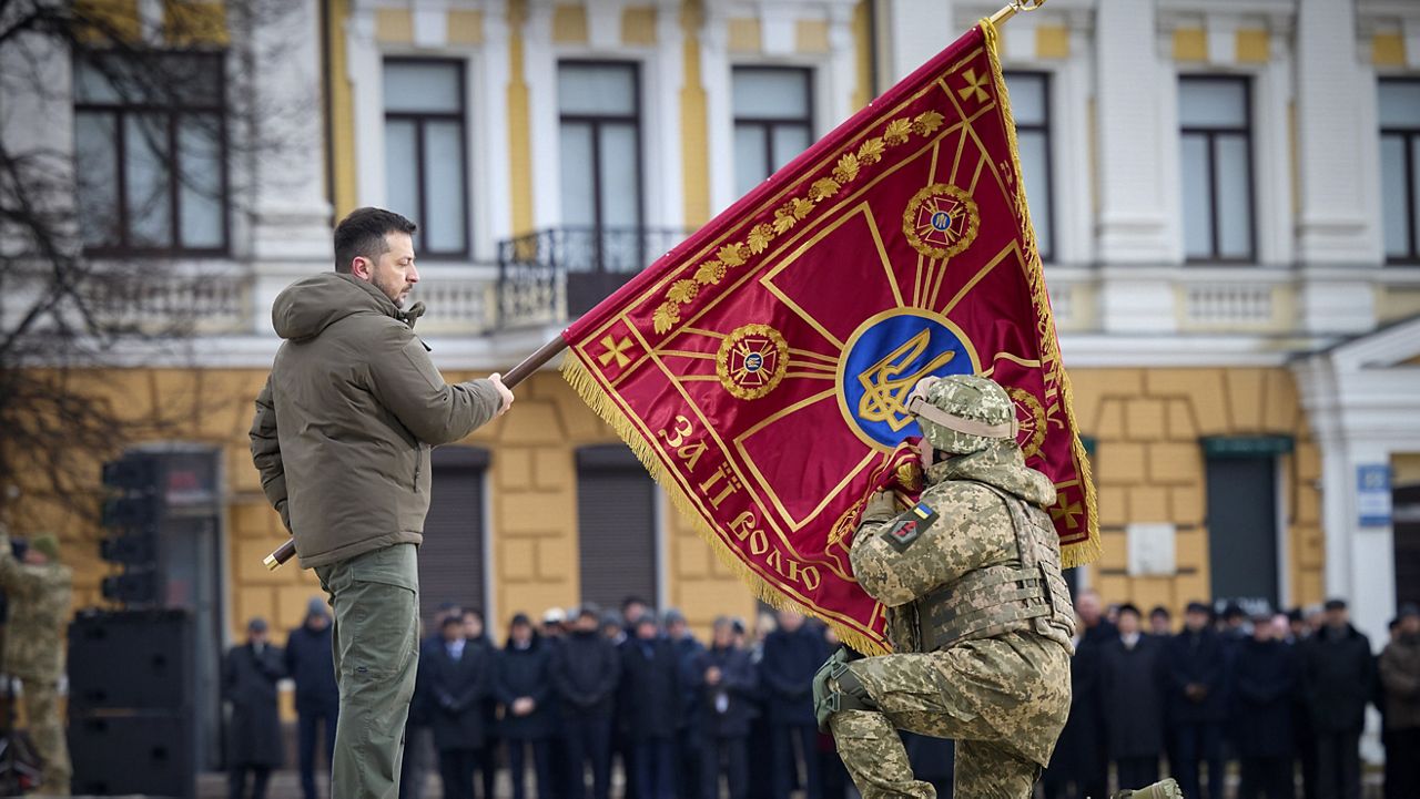 Ukrainian President Volodymyr Zelenskyy, left, holds the flag of a military unit as an officer kisses it, during a commemorative event in Kyiv, Ukraine, marking the one-year anniversary of the Russian invasion. (Ukrainian Presidential Press Office via AP)