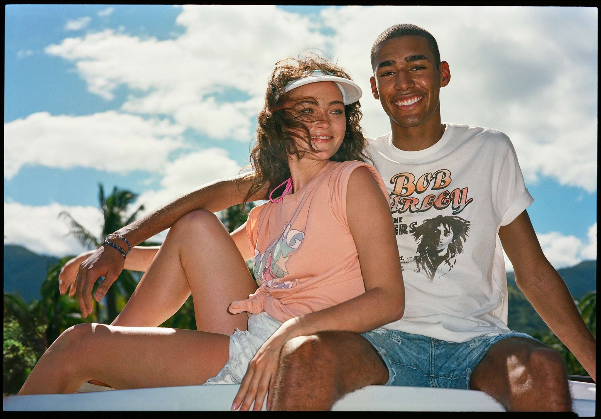 man and woman sitting on top of bus wearing AE denim shorts and graphic tees
