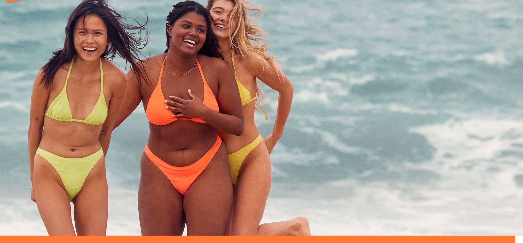 three women on beach wearing orange and yellow bikinis
