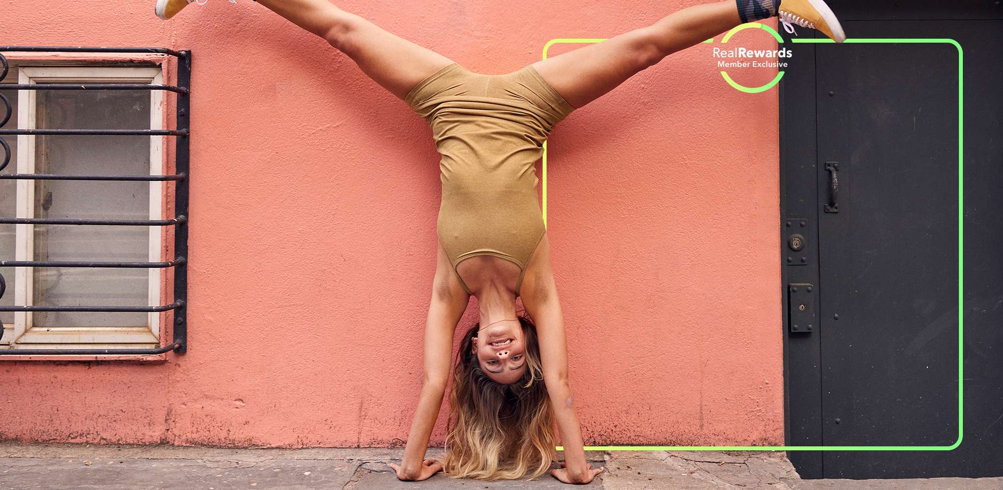 model in matching beige workout set doing a handstand in front of a pink wall