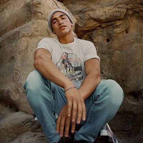 model crouching on rocks wearing AE jeans and graphic tee with beanie