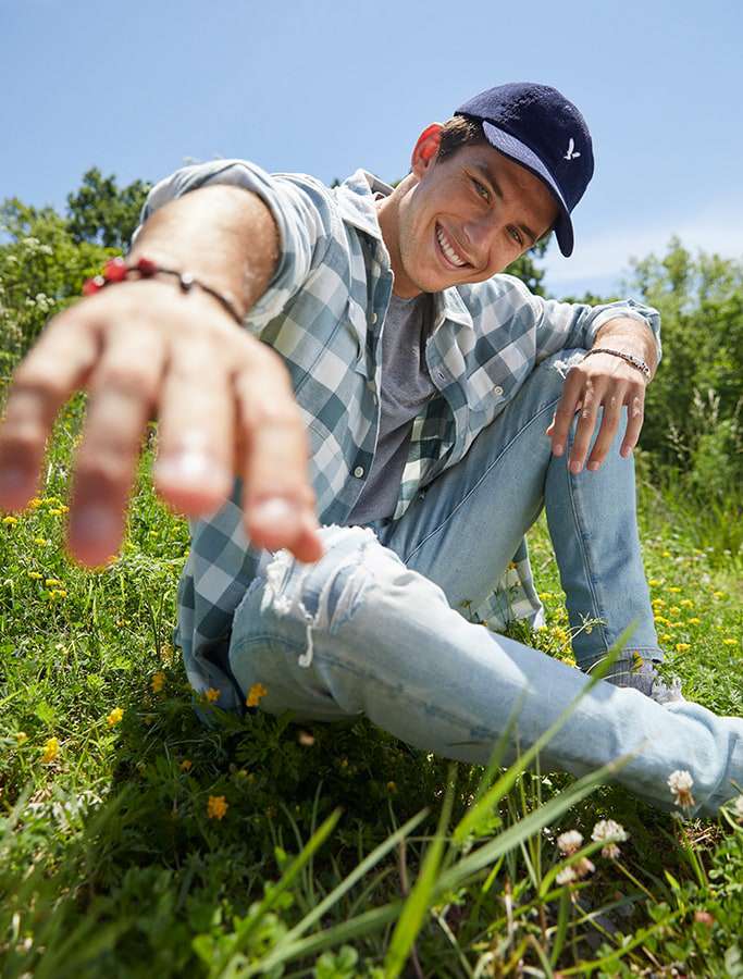 model in navy baseball cap, plaid button up top and light blue denim jeans