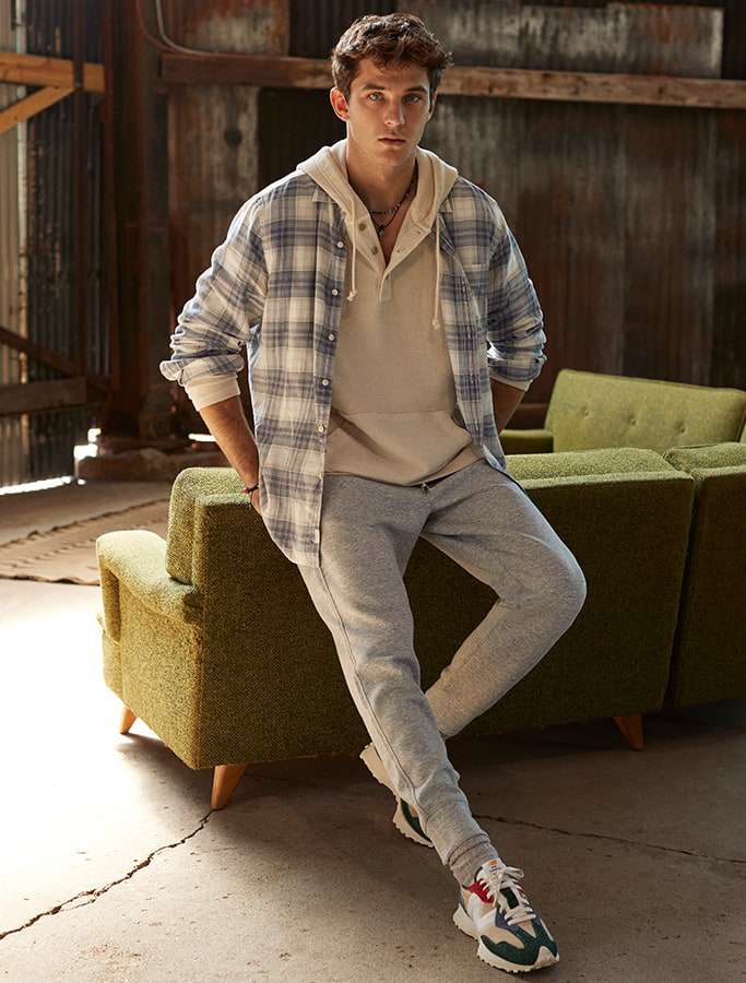 model in beige hoodie layered with plaid button up and grey joggers with sneakers