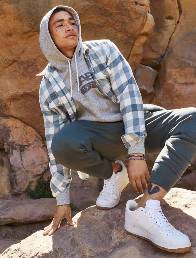 model in grey hoodie with plaid button up and grey joggers and white sneakers