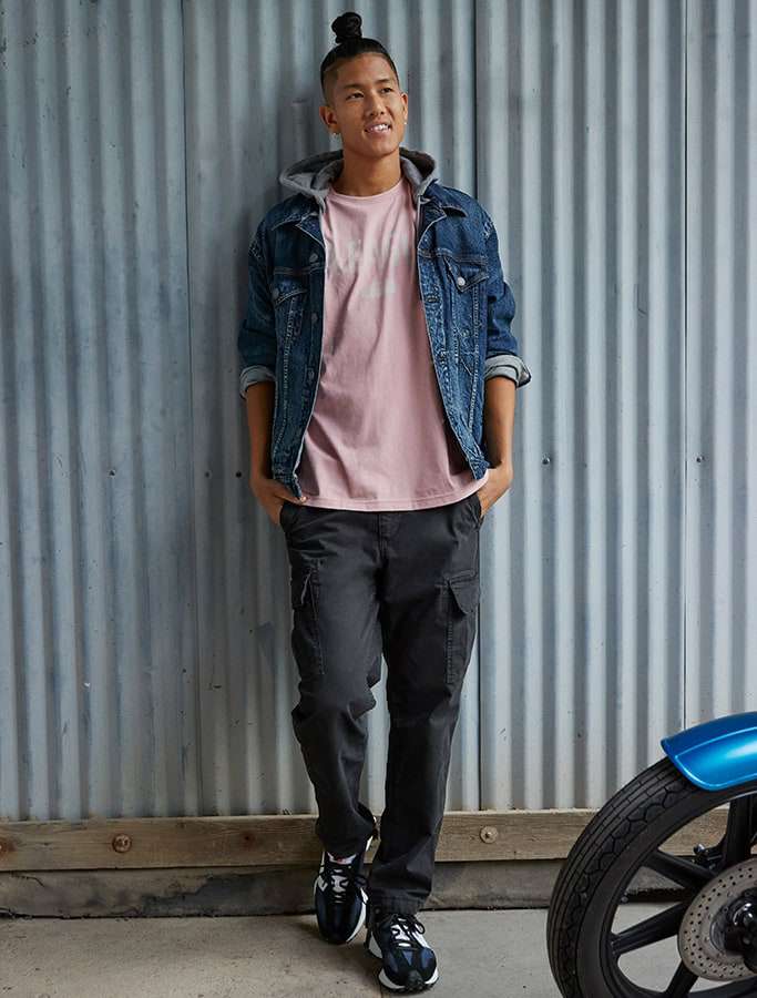 model in pink hoodie layered with denim jacket and black cargo pants