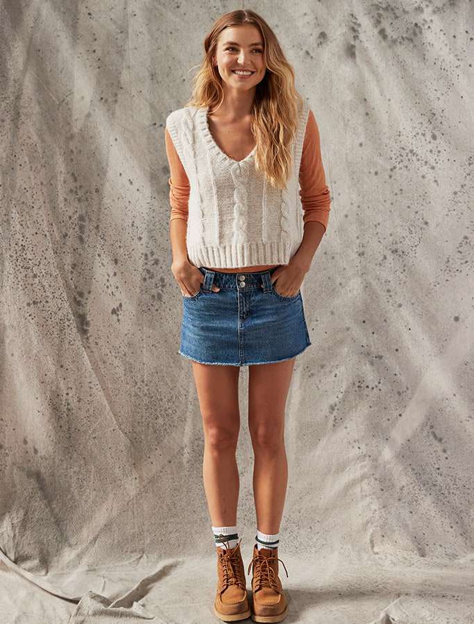 modle in cream sweater vest with denim skirt and high white socks with brown boots