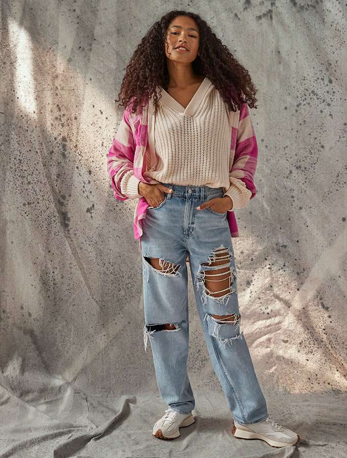 model in cream sweater with pink plaid outerwear and wearing destroyed denim pants with white sneakers