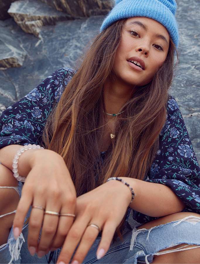 model sitting wearing ripped jeans, floral top, and blue beanie