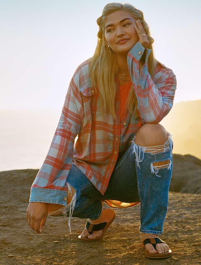 model crouched on the beach wearing flannel and ripped jeans