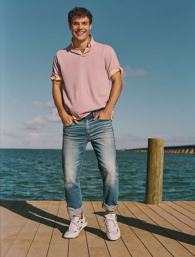 model in pink polo and denim jeans and white sneakers on a boardwalk