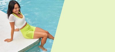 model sitting on the edge of the pool in a neon green workout set and white workout top layered