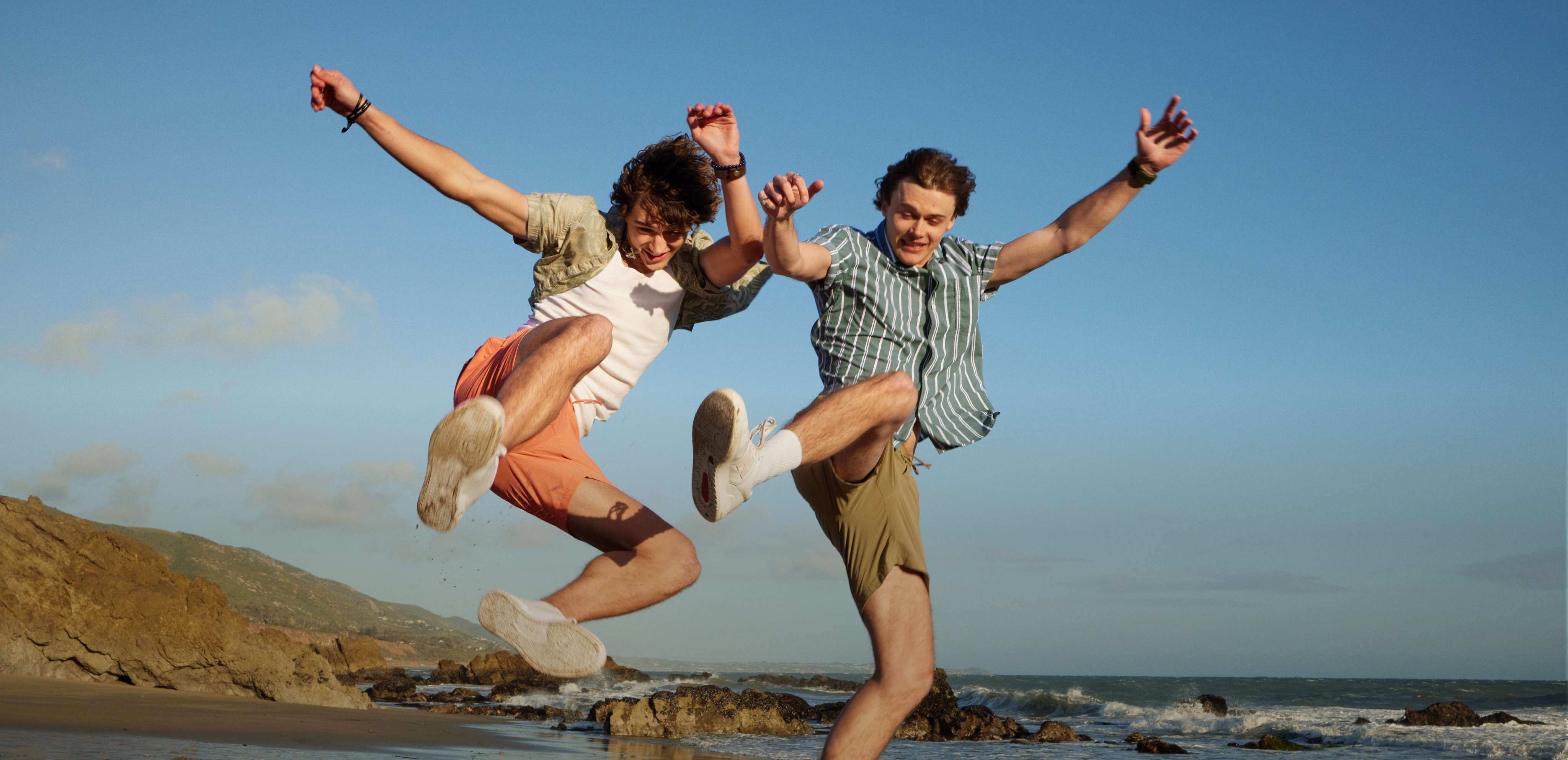 two models wearing AE shorts jumping in the air on a beach