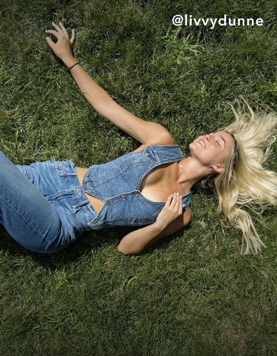 Model laying in grass with denim vest and jeans