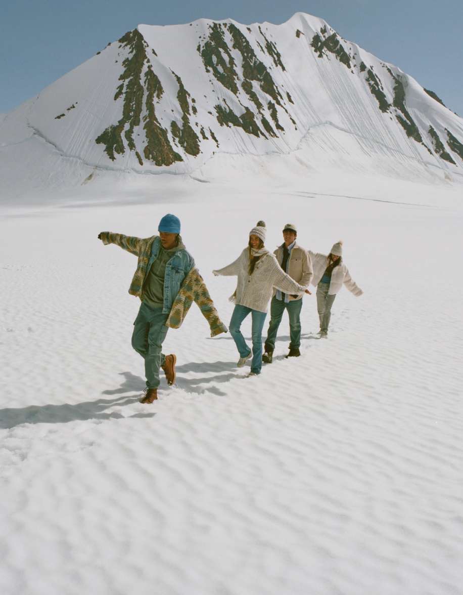 Modelos con AE prendas caminando en la nieve frente a una montaña