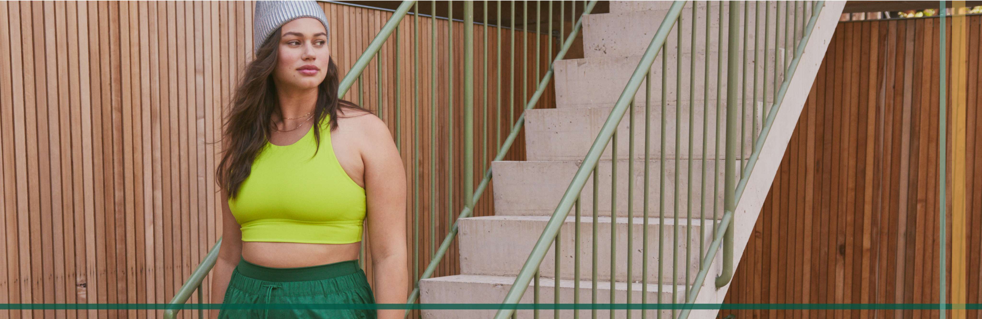 Model wearing neon green sports bra with green track pants and beanie