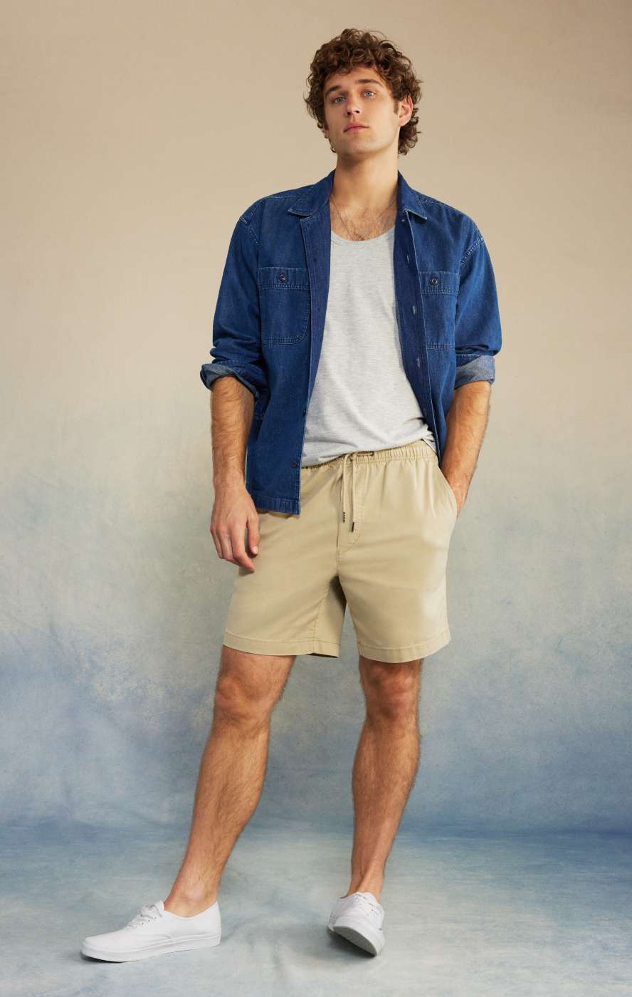 Model in tan shorts with white shirt and blue button up