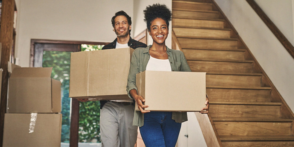Smiling couple carrying moving boxes indoors