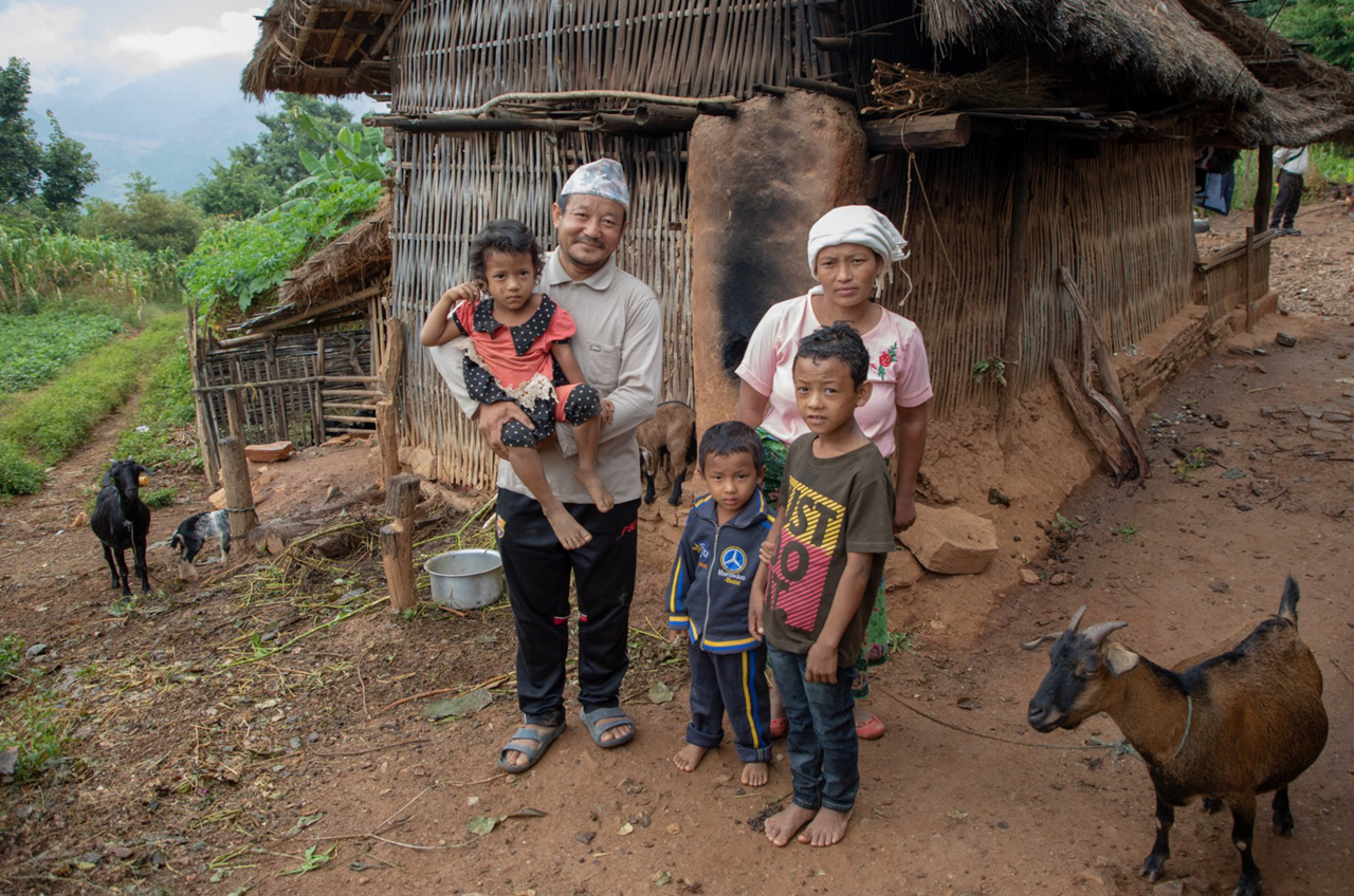 man and his family pose in front of hut