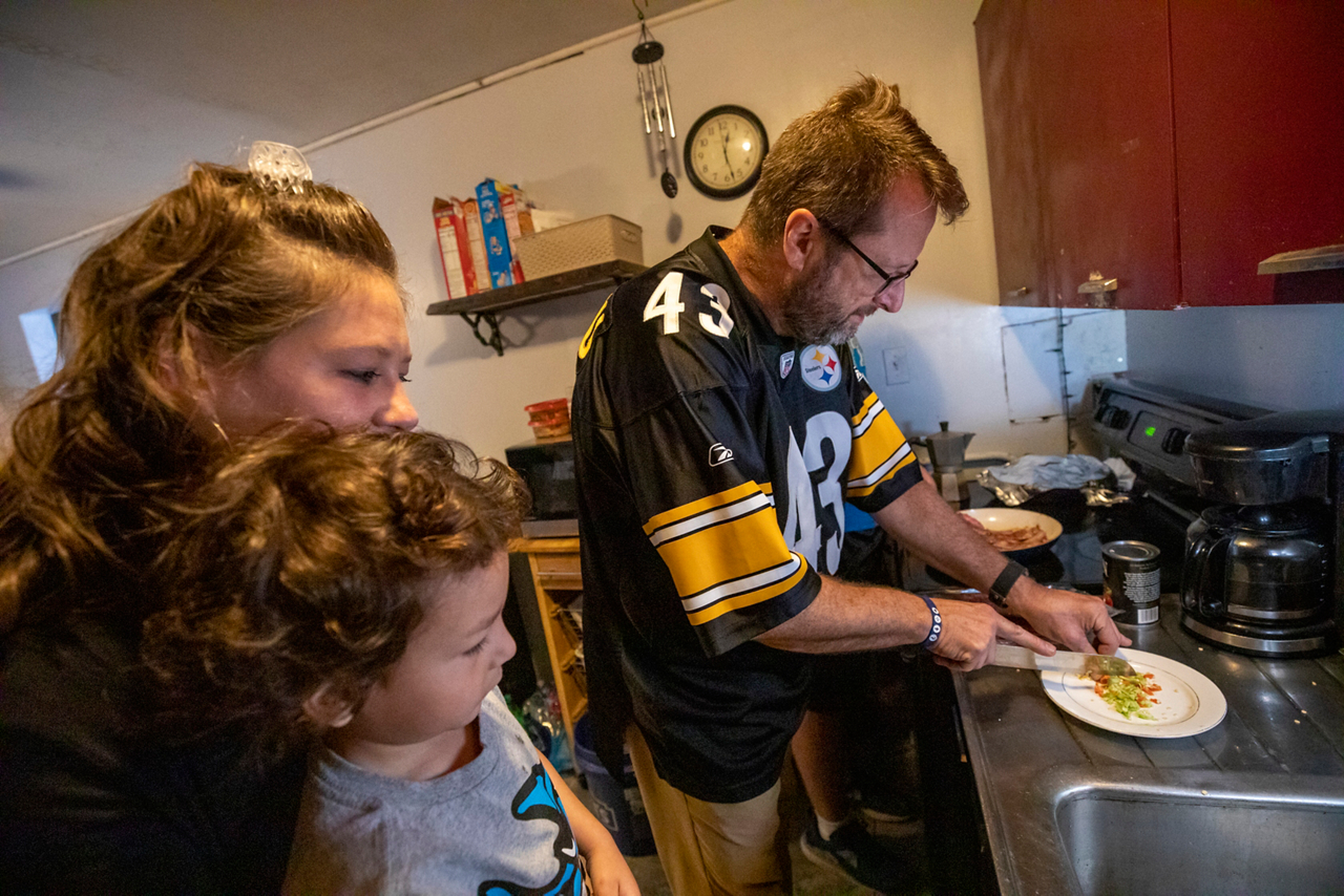 mother and son watch as old man cooks
