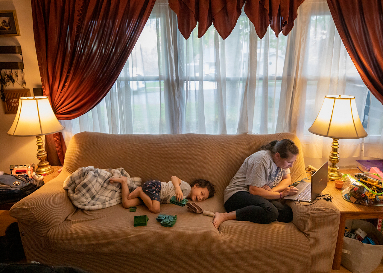 little boy plays on couch next to his mom as she works on her laptop