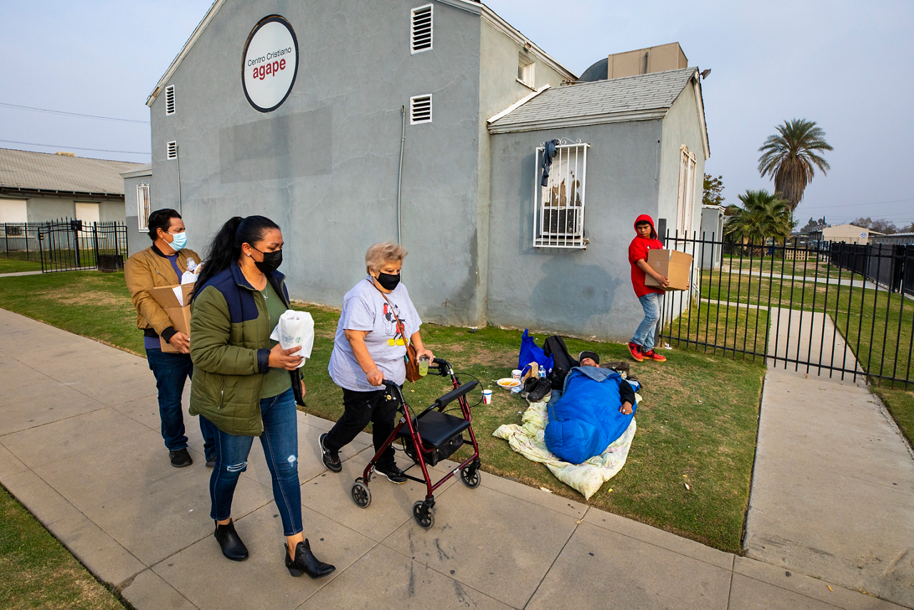 Jose and Rossana take a Box of Love® to a neighborhood resident’s car, walking past a homeless man who’d been given a bowl of soup earlier.