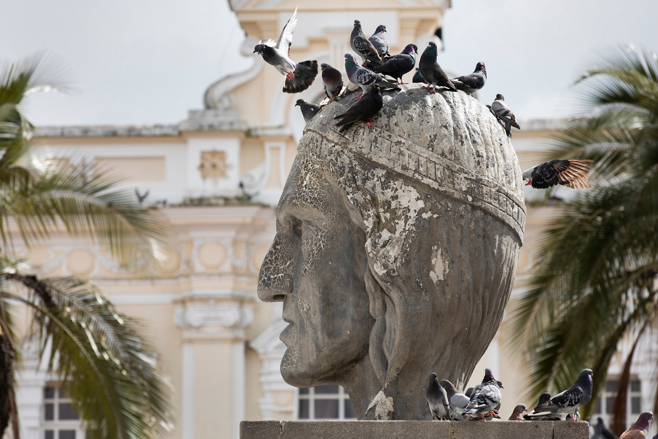A monument to Inca General Rumiñahui stands in the Otavalo city square, with the church Iglesia Catolica San Luis towering behind it.