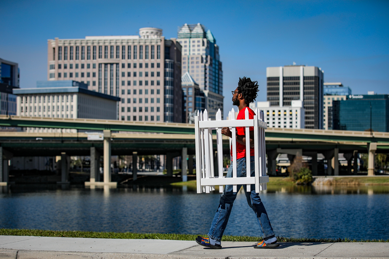 man carrying white picket fence through the city